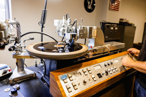 Mastering engineer standing beside lathe machine while a lacquer disc is being cut