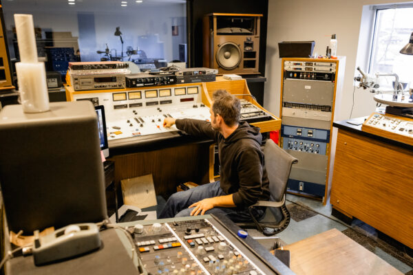 Mastering engineer in studio sitting in chair and adjusting volume control on the audio console