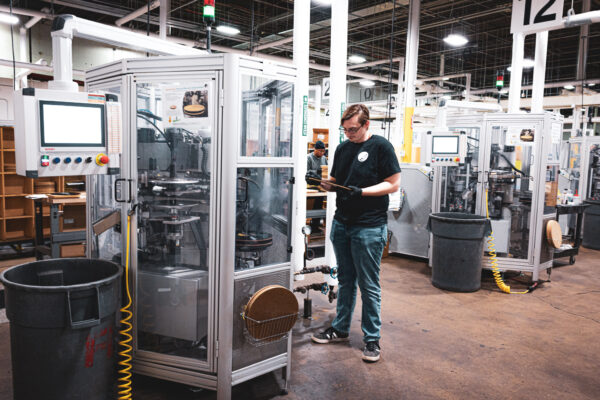 Worker standing beside a vinyl record press looking at a record