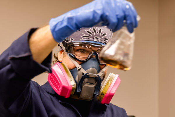 Plating employee wearing PPE and holding glass beaker of chemicals
